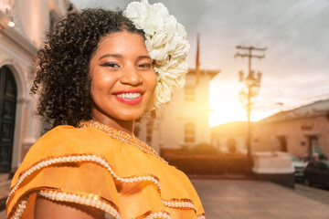 Mixed race teenager smiling wearing the classic Nicaraguan dress and flowers in her curly hair at sunset outside a colonial building - obrazy, fototapety, plakaty