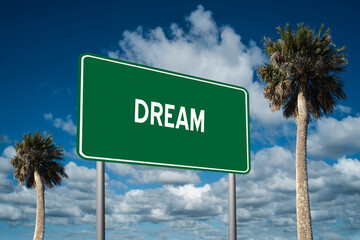 Fototapeta premium Highway sign with the word Dream on a beautiful blue sky background with palm trees. Motivational concept for finding what we want on the journey of life.