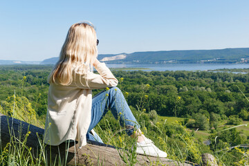 The concept of freedom and achievement of goals. The concept of a healthy lifestyle. A young girl is sitting on a mountain and admiring the view of the river and mountains. The girl enjoys the view.