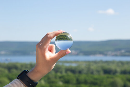 A look at the upside-down world through a ball. The girl's hand holds a crystal ball in which the image of mountains is inverted. Focus on the crystal ball. Take care of nature. Close-up