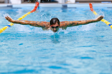 Young muscular man, professional swimmer in goggles training at public swimming-pool, outdoors. Sport, power, energy, style, hobby concept.