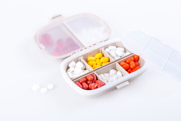 Pill box with colorful pills and vitamins. Plastic beige container with cells for medicines. Health concept. Selective focus, close-up.