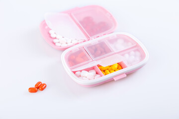 Pill box with colorful pills and vitamins. Plastic pink container with cells for medicines. Health concept. Selective focus, close-up.