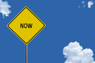 The word Now on a yellow road sign on a blue sky background.  Inspirational concept for success in life.