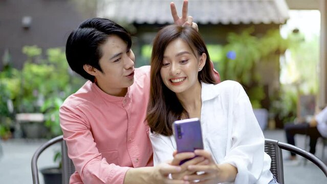 Happy asian couple spending time together at cafe, drinking coffee and posing taking selfie together in a happy and fun mood. Smiling man and woman photographing on mobile having coffee break.