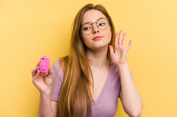 Young caucasian woman holding car keys isolated on yellow background trying to listening a gossip.