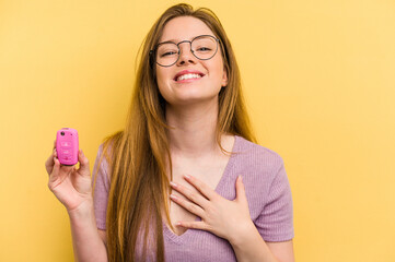 Young caucasian woman holding car keys isolated on yellow background laughs out loudly keeping hand on chest.