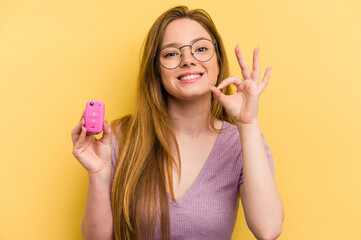 Young caucasian woman holding car keys isolated on yellow background cheerful and confident showing ok gesture.