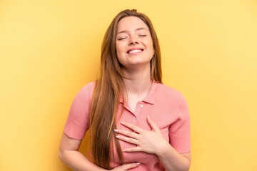 Fototapeta premium Young caucasian woman isolated on yellow background laughs happily and has fun keeping hands on stomach.