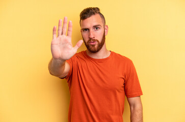 Young caucasian man isolated on yellow background standing with outstretched hand showing stop sign, preventing you.