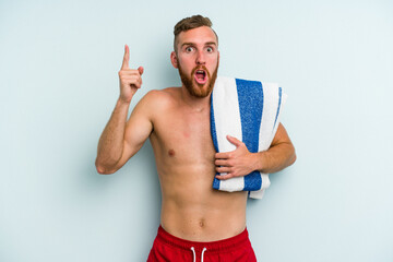 Young caucasian man going to the beach holding a towel isolated on blue background having an idea, inspiration concept.