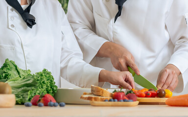 Selective focus on hands of professional chef wearing white uniform, using knife, cutting vegetable, cooking and preparing healthy food or meal for restaurant or hotel service.