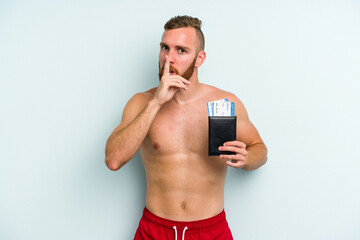 Fototapeta premium Young caucasian man holding a passport isolated on blue background keeping a secret or asking for silence.