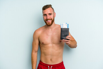 Fototapeta premium Young caucasian man holding a passport isolated on blue background happy, smiling and cheerful.
