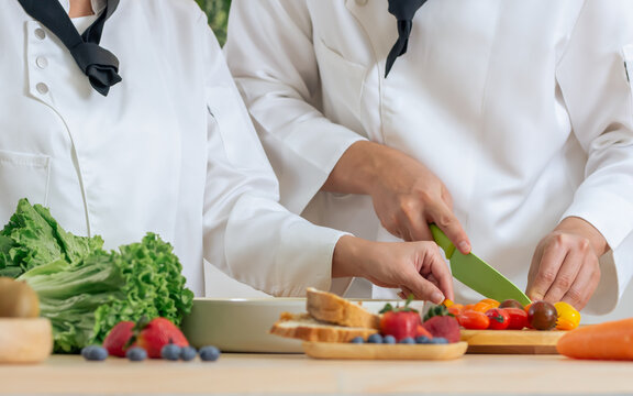 Selective focus on hands of professional chef wearing white uniform, using knife, cutting vegetable, cooking and preparing healthy food or meal for restaurant or hotel service. - Powered by Adobe