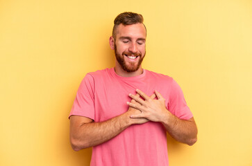 Young caucasian man isolated on yellow background laughing keeping hands on heart, concept of happiness.