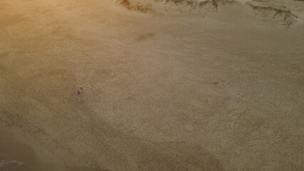 Three friends walking on beach with deck chairs at sunset, Playa La Viuda in Uruguay. Aerial top-down view. Going home
