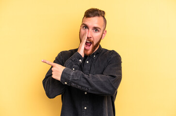 Young caucasian man isolated on yellow background saying a gossip, pointing to side reporting something.