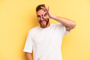Fototapeta na wymiar Young caucasian man isolated on yellow background excited keeping ok gesture on eye.