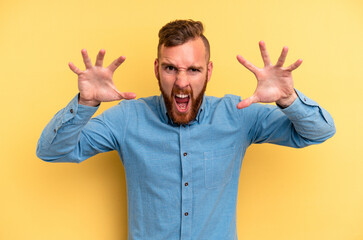 Naklejka premium Young caucasian man isolated on yellow background showing claws imitating a cat, aggressive gesture.
