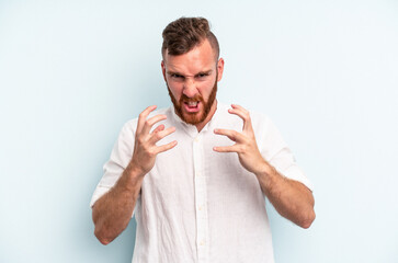 Young caucasian man isolated on blue background upset screaming with tense hands.