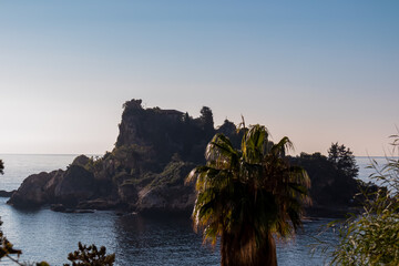 Panoramic morning view from the beach on the small magical island Isola Bella in Taormina, Sicily, Italy, Europe, EU. Paradise landscape at Mediterranean sea. Calm water surface Ionian sea. Palm tree