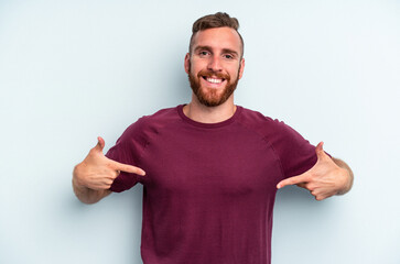 Fototapeta premium Young caucasian man isolated on blue background person pointing by hand to a shirt copy space, proud and confident