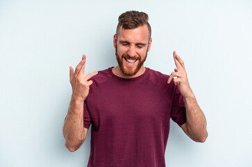 Naklejka premium Young caucasian man isolated on blue background crossing fingers for having luck