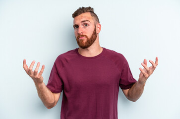 Naklejka premium Young caucasian man isolated on blue background doubting and shrugging shoulders in questioning gesture.
