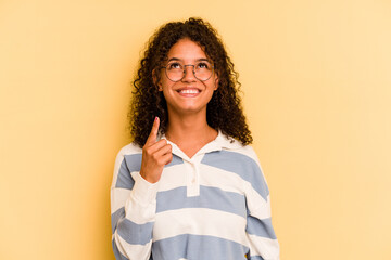 Young Brazilian woman isolated on yellow background indicates with both fore fingers up showing a...