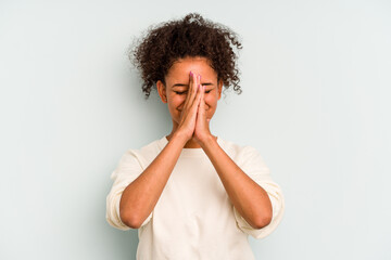 Young Brazilian woman isolated on blue background holding hands in pray near mouth, feels confident.