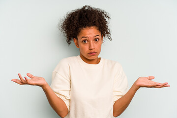 Young Brazilian woman isolated on blue background doubting and shrugging shoulders in questioning...