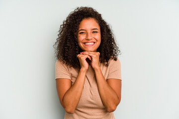 Young Brazilian woman isolated on blue background keeps hands under chin, is looking happily aside.