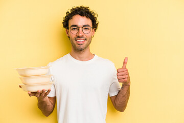 Young caucasian man holding tupper isolated on yellow background smiling and raising thumb up