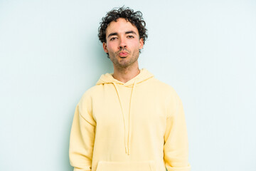 Young caucasian man isolated on blue background blows cheeks, has tired expression. Facial expression concept.