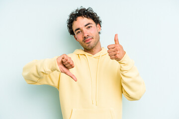 Young caucasian man isolated on blue background showing thumbs up and thumbs down, difficult choose...