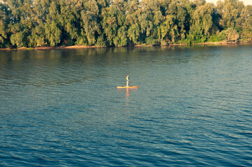 Young man swimming on sup board alone at sunset.