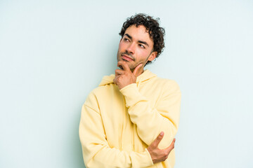 Fototapeta premium Young caucasian man isolated on blue background thinking and looking up, being reflective, contemplating, having a fantasy.