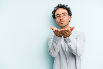 Young caucasian man isolated on blue background folding lips and holding palms to send air kiss.