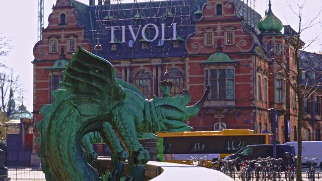Bronze statue depicting a chimera dragon with one of the entrances to the Tivoli gardens amusement park behind it. Copenhagen, Denmark, Europe