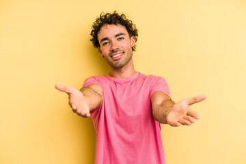 Young caucasian man isolated on yellow background showing a welcome expression.