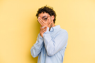 Fototapeta na wymiar Young caucasian man isolated on yellow background blink through fingers frightened and nervous.