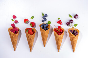 Waffle cones with fresh summer berries. Berry gelato, ice cream concept with raspberry, strawberry,  blueberry, cherry, currant in waffle cones on a white background