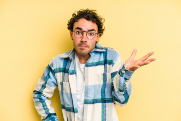 Young caucasian man isolated on yellow background doubting and shrugging shoulders in questioning...
