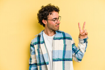 Naklejka premium Young caucasian man isolated on yellow background joyful and carefree showing a peace symbol with fingers.