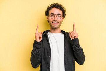 Young caucasian man isolated on yellow background indicates with both fore fingers up showing a...
