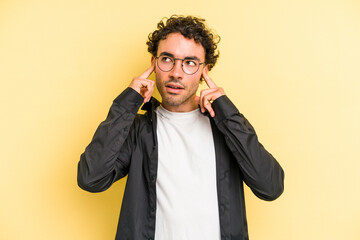 Young caucasian man isolated on yellow background covering ears with fingers, stressed and desperate by a loudly ambient.
