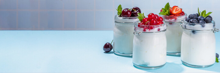 Variety of yogurts in portion glass jars. Healthy summer breakfast concept, with seasonal berry – strawberry, cherry, blueberry, currant 