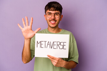 Young hispanic man holding meta verse placard isolated on purple background smiling cheerful showing number five with fingers.