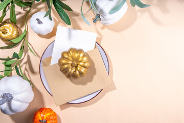 Fall seasonal table setting flatlay. Autumn seasonal holidays background in beige colors. White, orange, golden pumkins decor for thanksgiving, fall holidays, invitation menu background